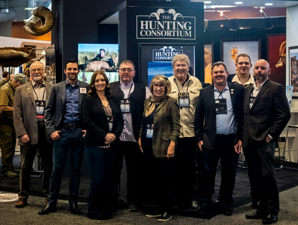 The Hunting Consortium team standing at the company’s trade show booth beneath The Hunting Consortium logo.