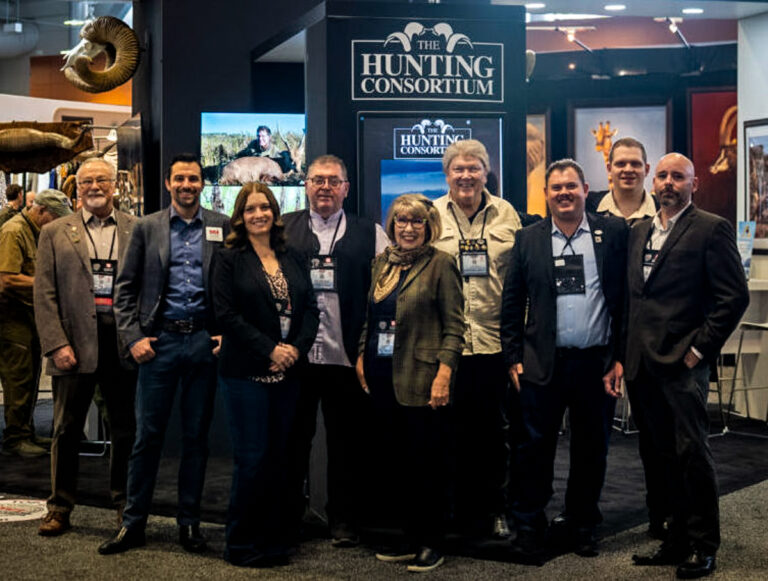 The Hunting Consortium team standing at the company’s trade show booth beneath The Hunting Consortium logo.